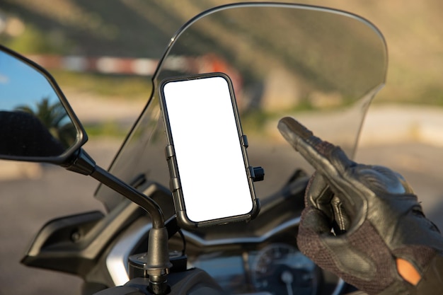 Primer plano de la mano de un motociclista apuntando a la pantalla en blanco con una maqueta de su teléfono inteligente montado en el scooter