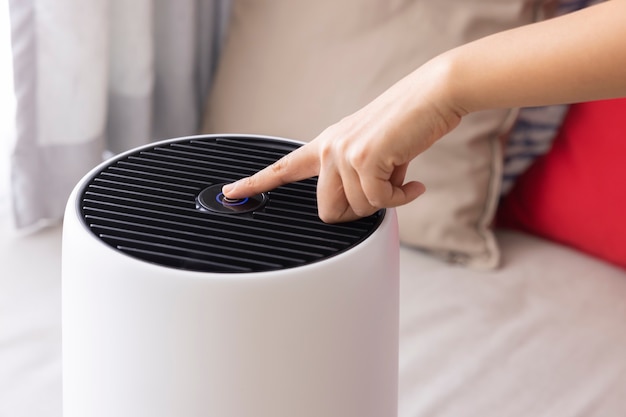 Foto primer plano de la mano de la mujer asiática presionando un botón en la máquina purificadora de aire en un dormitorio proteger pm 25