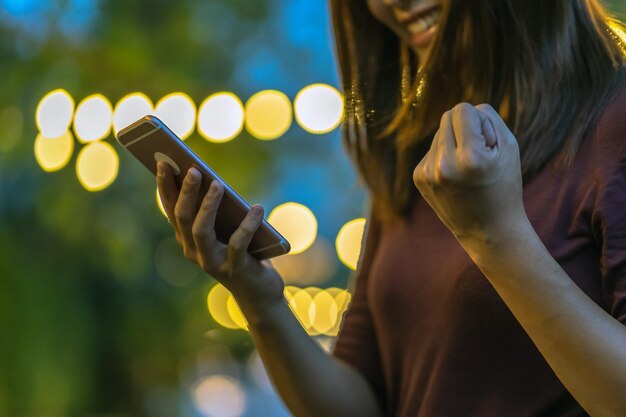 Foto primer plano de la mano de una mujer asiática usando un teléfono inteligente y celebrando en un negocio de parque al aire libre