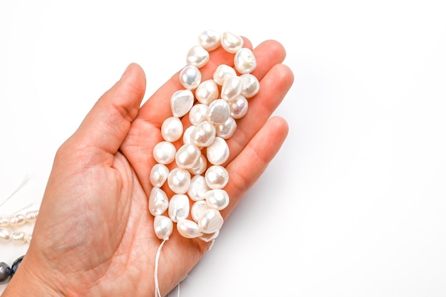 Primer plano de la mano de la mujer con una cadena de perlas barrocas blancas aisladas en blanco. Mano sujetando recortadas p