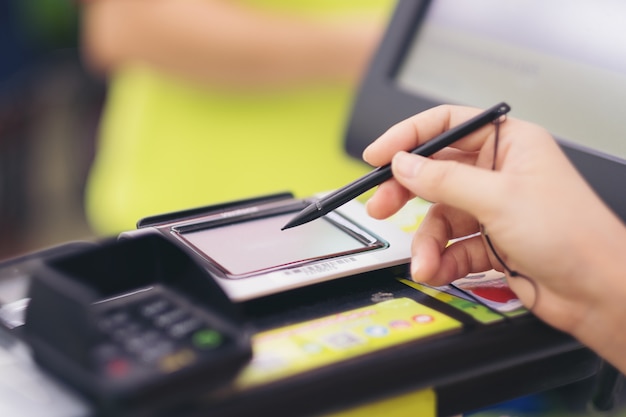 Foto primer plano de la mano de la mujer consumidora firmando en una pantalla táctil de tarjeta de crédito