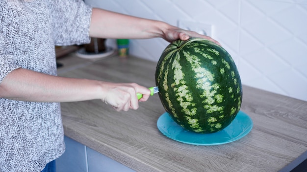 Primer plano de la mano de mujer cortando sandía fresca en la cocina