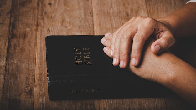 Foto el primer plano de la mano de una mujer cristiana en la sagrada biblia es orar y adorar gracias a dios en la iglesia con un concepto de fondo negro para la fe, la espiritualidad y la religión