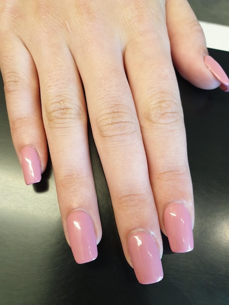 Primer plano de la mano de una mujer con esmalte de uñas rosa en la mesa