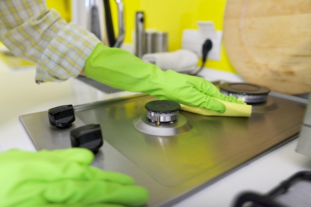 Foto primer plano de la mano de una mujer con guantes protectores de goma haciendo limpieza en la cocina lavando la encimera de la estufa de gas