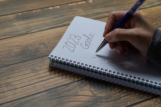 Primer plano de la mano de una mujer joven escribiendo en un cuaderno sus resoluciones de Año Nuevo para 2023