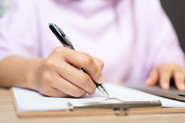 Primer plano Mano de mujer de negocios escribiendo documentos de firma en papel en el escritorio de la oficina