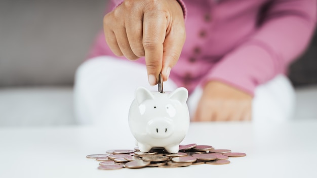 Primer plano de la mano de la mujer de negocios poniendo monedas de dinero en la hucha para ahorrar dinero. Ahorro de dinero y concepto financiero.