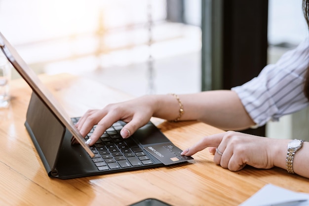 Primer plano de una mano de mujer de negocios usando un teclado de tableta para comprar en línea con una tarjeta de crédito en la mesa