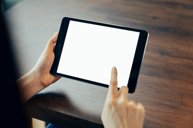 Primer plano de la mano de la mujer que sostiene la tableta digital sobre la mesa y la pantalla está en blanco.