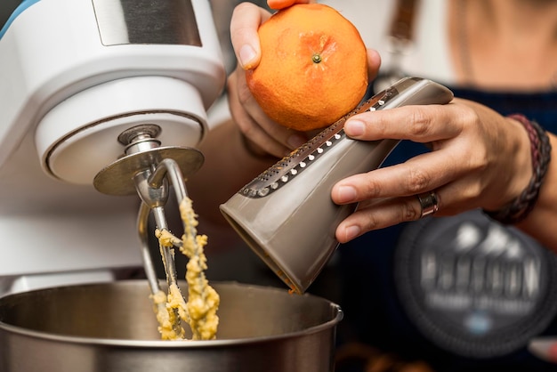 Primer plano de la mano de una mujer rallando una naranja en un tazón de una batidora eléctrica para la preparación de la receta casera de alfajores argentinos