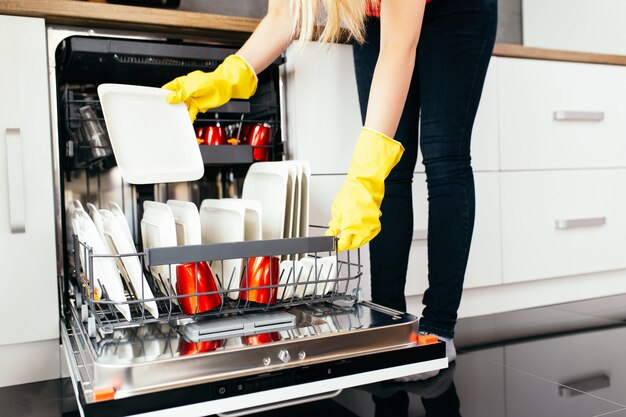 Primer plano de la mano de la mujer sacando platos limpios de la máquina lavavajillas.