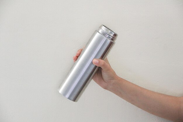 Primer plano de la mano de una mujer sosteniendo una botella de agua termoecológica de acero inoxidable reutilizable gris con mocku