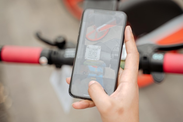 Primer plano de la mano de la mujer usando la aplicación móvil, escaneando el código QR para alquilar un scooter eléctrico