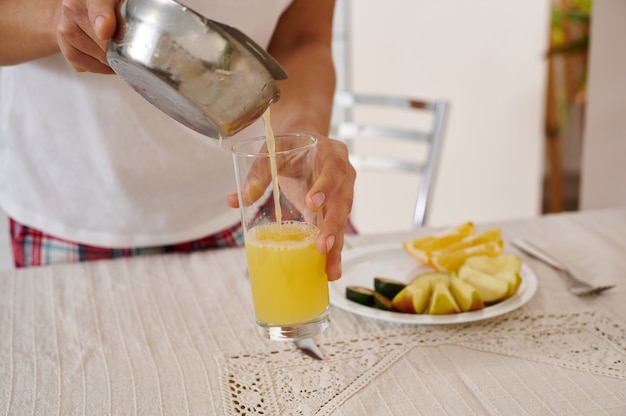 Primer plano de la mano de una mujer vertiendo jugo de naranja recién exprimido de prensa de cítricos en un vaso transparente. Preparando el desayuno