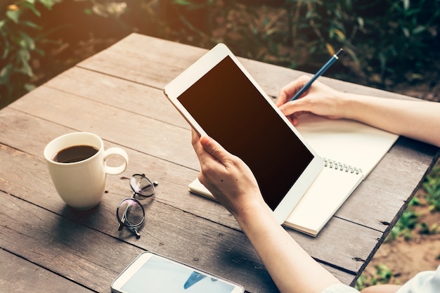 Primer plano de la mano de las mujeres que sostienen la computadora de la tableta con la pantalla en blanco del espacio de la copia para su publicidad. Mujer de la mano que usa la tableta en cafetería.