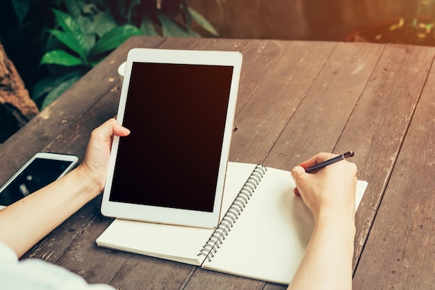 Primer plano de la mano de las mujeres que sostienen la computadora de la tableta con la pantalla en blanco del espacio de la copia para su publicidad. Mujer de la mano que usa la tableta en cafetería.