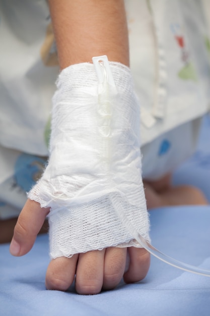 Foto primer plano mano de niño enfermo con el agua salada tubo en la cama en el hospital