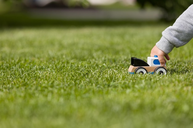 Primer plano de la mano de un niño jugando con un cayo de juguete en la hierba verde del parque Niño pequeño jugando con un coche pequeño Guardería y guardería Al aire libre Infancia y concepto de estilo de vida Actividades para niños