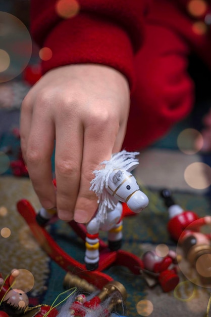 Primer plano de la mano de un niño jugando con la figurilla de un caballito. Decoración para un árbol de Navidad.