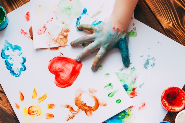 Primer plano de la mano del niño pintando colorido mosaico Kid está dibujando su palma en hojas blancas con pinturas