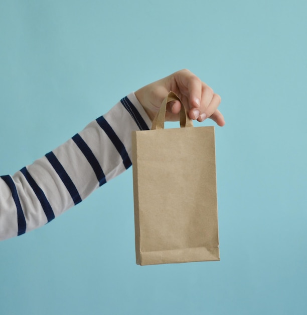 Primer plano de la mano de un niño sosteniendo una bolsa de kraft sobre un fondo azul El concepto de embalaje ecológico