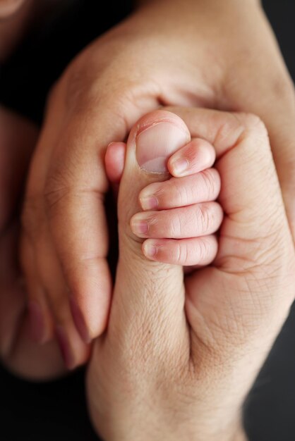 Primer plano de la mano pequeña del niño y la mano de la madre y el padre Un bebé recién nacido después del nacimiento se aferra fuertemente al dedo de sus padres Fotografía macro profesional sobre fondo negro