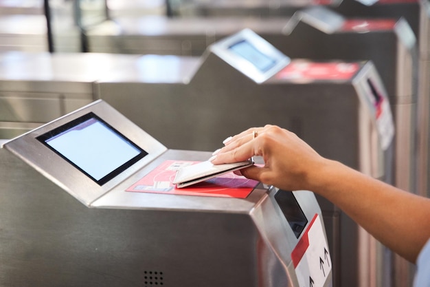 Primer plano de la mano de una persona irreconocible con una tarjeta de acceso que entra por las puertas de seguridad de un sistema de transporte público