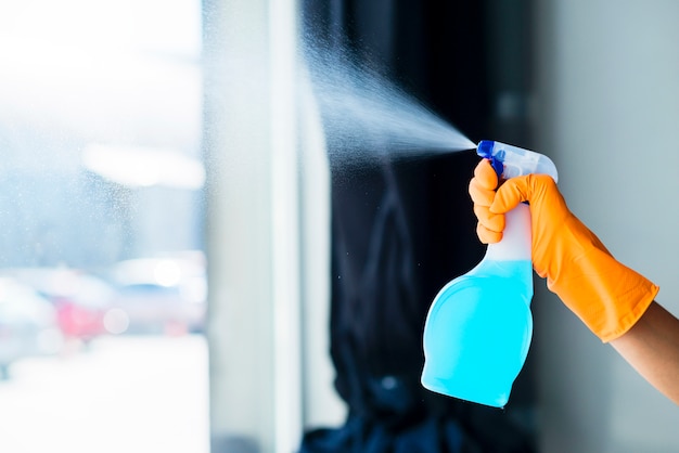 Primer plano de la mano de una persona rociando el detergente líquido en el vidrio de la ventana