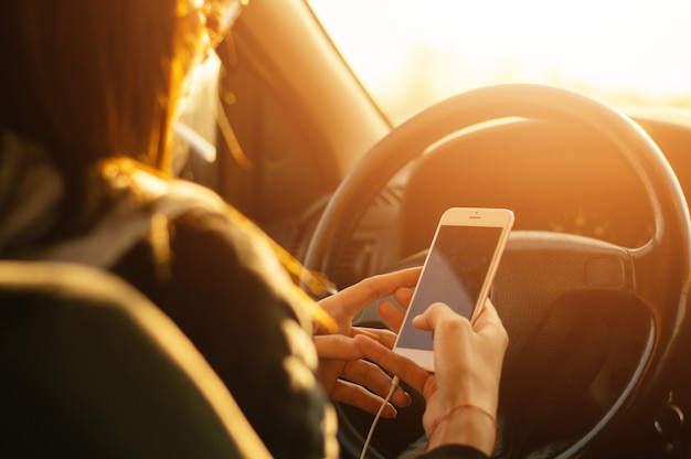 Primer plano de la mano de una persona usando un teléfono celular en un automóvil en la puesta de sol, destello de lente