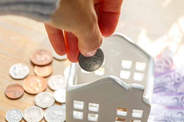 Foto primer plano de la mano poniendo una moneda en la alcancía de la casa de cerámica