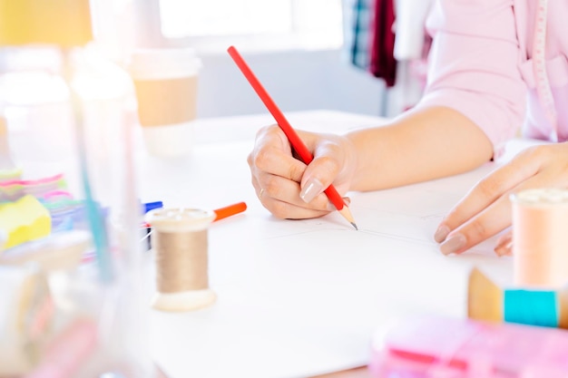 Primer plano de la mano que sostiene el diseño de dibujo a lápiz sobre papel Un escritorio de trabajo con muchos accesorios para coser corte de tela