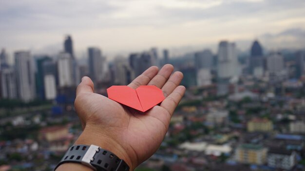 Foto primer plano de la mano que sostiene la forma de un corazón contra el paisaje urbano