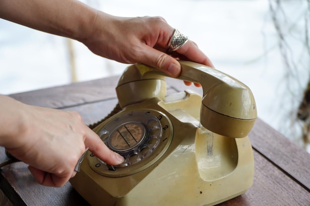 Primer plano de la mano que sostiene el viejo teléfono rotatorio negro y marcando un número con polvo en el teléfono encendido