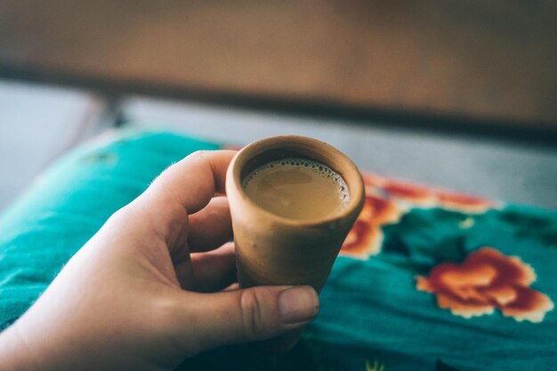 Foto primer plano de una mano recortada sosteniendo café en una taza de arcilla