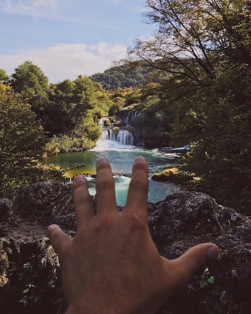 Foto primer plano de la mano sobre la roca contra la cascada en el bosque