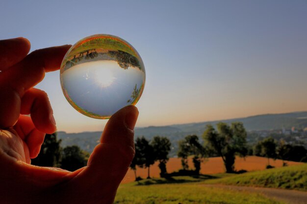 Primer plano de la mano sosteniendo una bola de cristal contra el cielo durante la puesta del sol