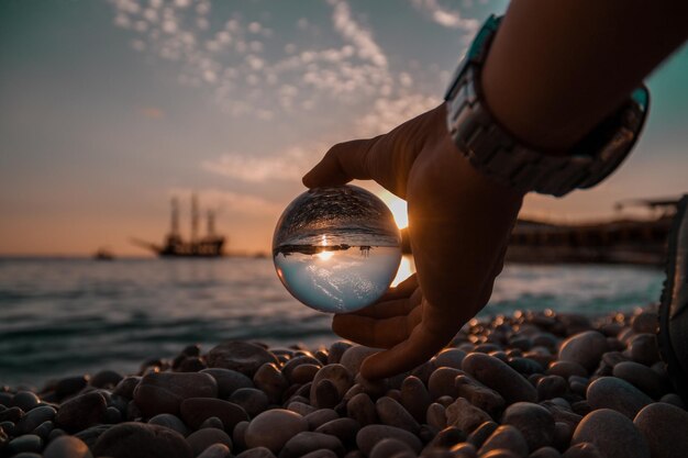 Foto primer plano de una mano sosteniendo una bola de cristal en la playa durante la puesta de sol