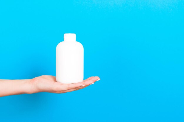 Primer plano de la mano sosteniendo la botella contra un fondo azul