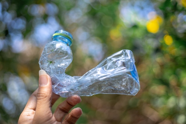 Foto primer plano de la mano sosteniendo una botella de plástico contra los árboles