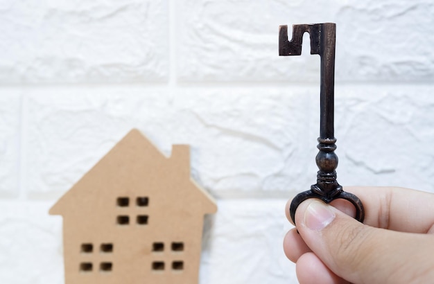 Primer plano de una mano sosteniendo una casa de madera contra un edificio