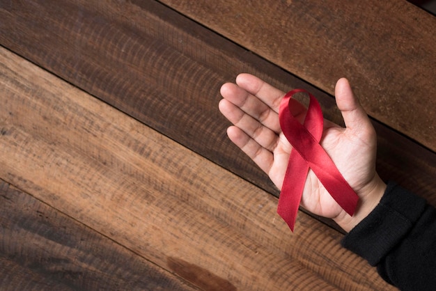 Primer plano de una mano sosteniendo una cinta roja sobre una mesa de madera