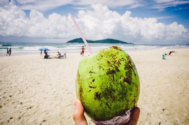 Foto primer plano de una mano sosteniendo un coco en la playa