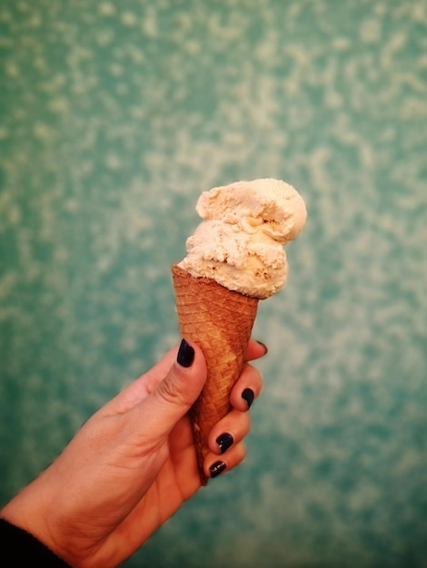 Foto primer plano de la mano sosteniendo un cono de helado contra un fondo borroso