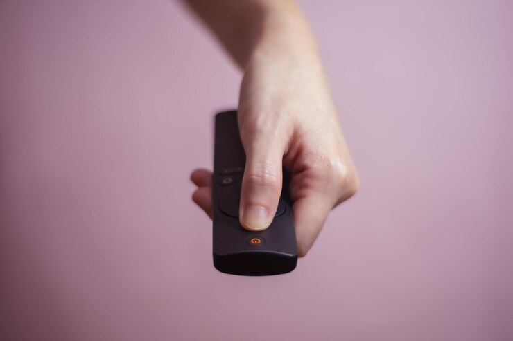 Foto primer plano de la mano sosteniendo el control remoto contra un fondo rosado