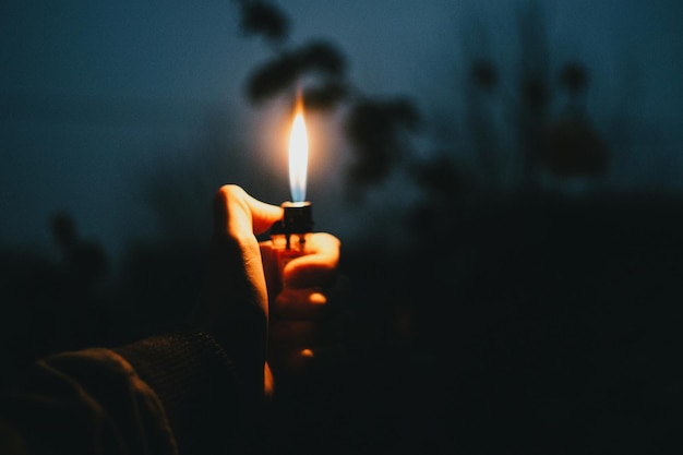 Foto primer plano de una mano sosteniendo un encendedor de cigarrillos iluminado