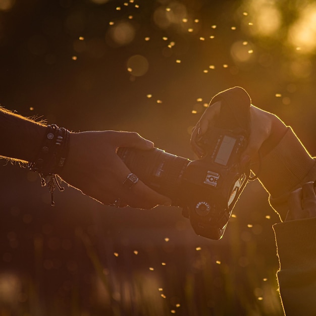 Foto primer plano de la mano sosteniendo la foto de la cámara en las manos a la luz del atardecer