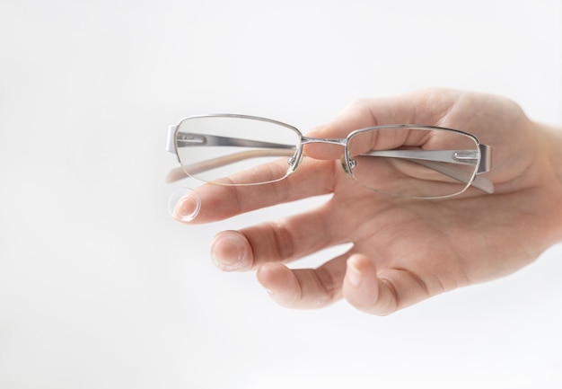 Primer plano de la mano sosteniendo gafas contra un fondo blanco