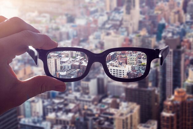 Primer plano de la mano sosteniendo gafas contra el paisaje urbano