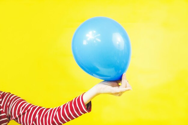 Foto primer plano de la mano sosteniendo globos contra un fondo amarillo